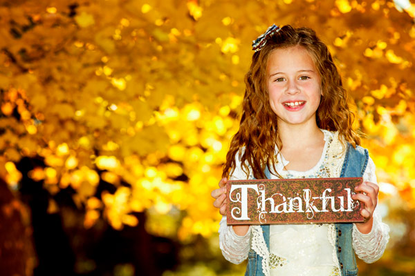 Girl holding "thankful" sign to show how lay therapy can foster gratitude with Butterfly Beginnings Play Therapy