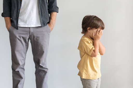 Image of young child with face in hands in front of dad with hands in pockets for butterfly beginnings play therapy in eastern iowa blog: Parental Invalidation